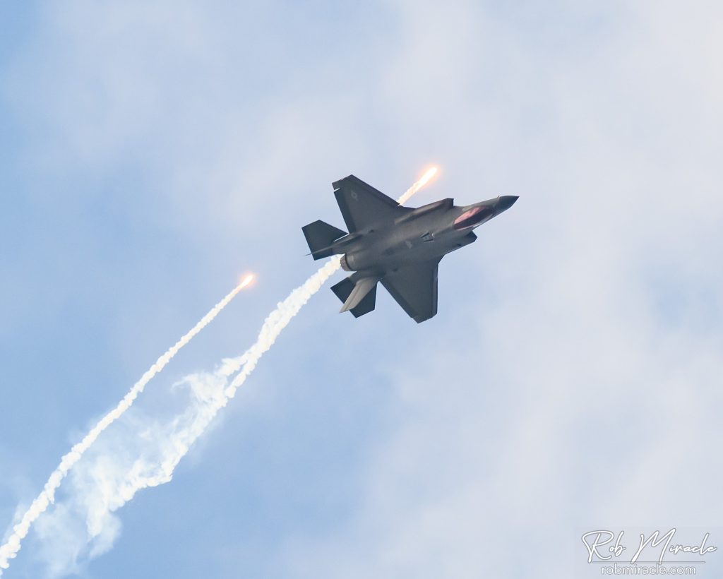 A F-35A stealth fighter flies upside down during an airshow while deploying flairs
