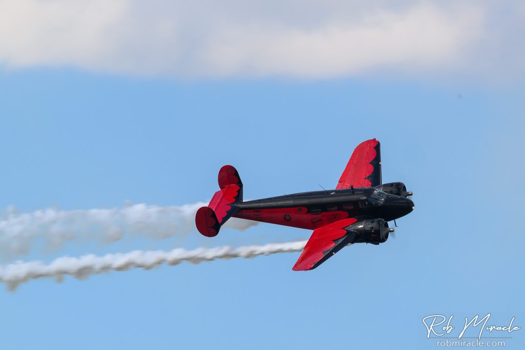 A red and black twin-engine plane from the past flies through the air.