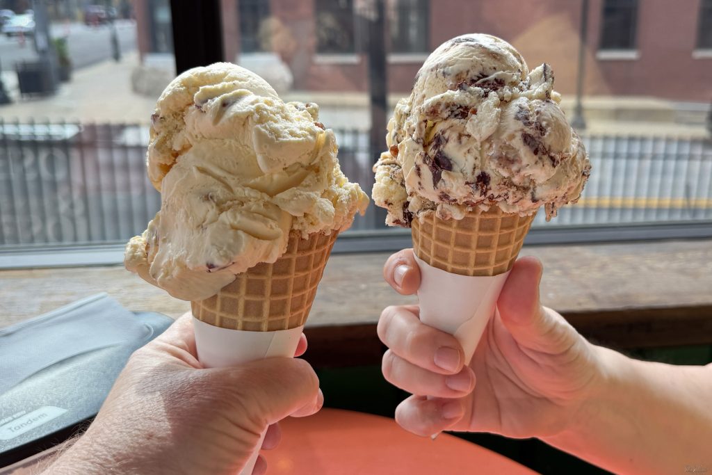 Two ice cream cones with multiple scoops of ice cream each in two people's hands.