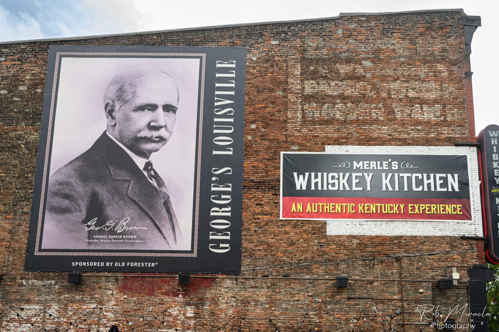 The side of Merle's Whisky Kitchen with a banner dedicated to Geroge Brown, found of Brown-Forman, and distributor of the Old Forrester brand of Bourbon.