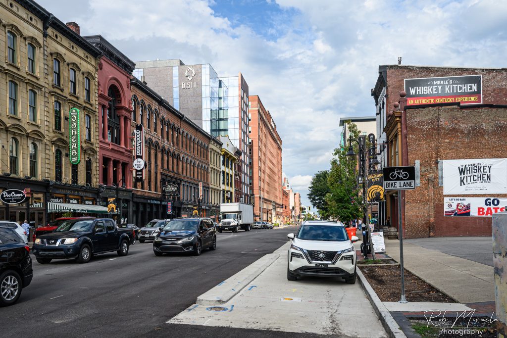 View down Whiskey Row/Main Street in Louisville Kentucky. Old buildings and some new line the street beneath a partly cloudy sky.